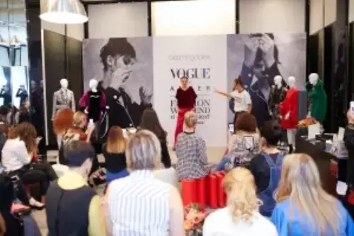 This is a snapshot from one of our fashion events with a model showing the fashion, an instructor presenting it, and a crowd listening and taking photos.
