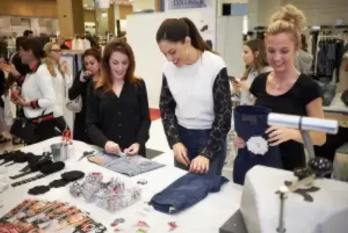 The image shows a group of ladies at one of our fashion events, inspecting the products.